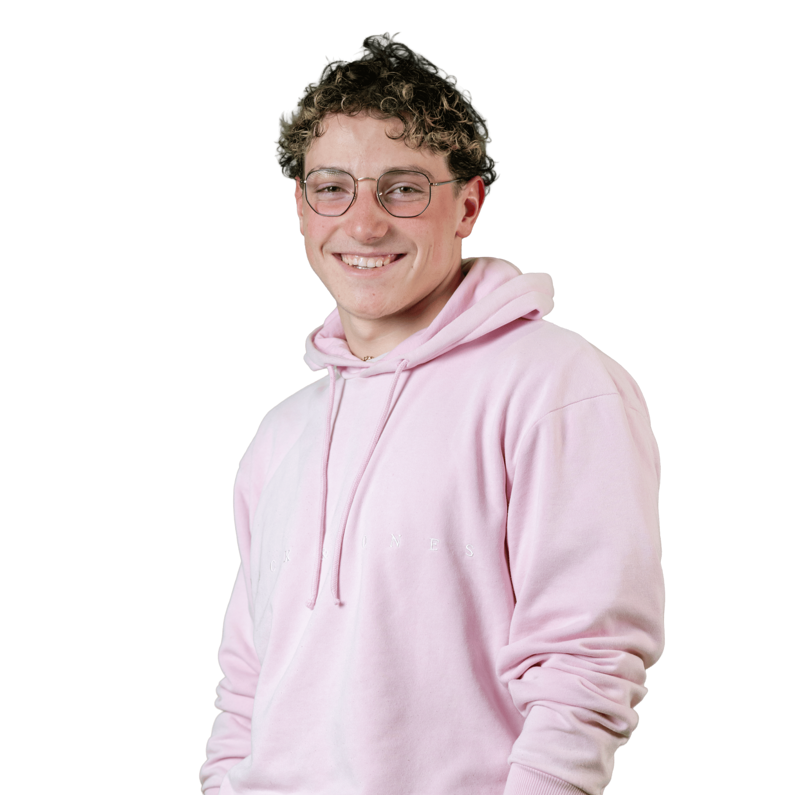 Jeune personne souriante, aux cheveux courts et bouclés, portant des lunettes rondes et un sweat à capuche rose pâle, debout devant un fond blanc uni.